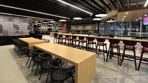 A modern restaurant with a long wooden table and black chairs, surrounded by a bar area with stools. - Hilton Dallas Lincoln Centre by the Galleria (Dallas)