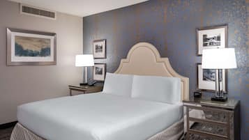 Una habitación de hotel con una cama grande, dos mesitas de noche con lámparas, un cabecero y cuadros enmarcados en las paredes.
