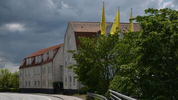 Ein Gebäude mit rotem Ziegeldach und zahlreichen Fenstern, umgeben von Grünflächen und einer gewundenen Straße.