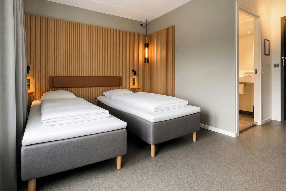 A hotel room with two beds, a wooden headboard, and a wall-mounted light fixture.