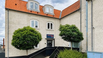 A building with a brick facade, a red-tiled roof, and a staircase leading to the entrance.