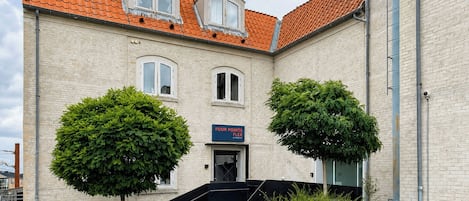 A building with a brick facade, a red-tiled roof, and a staircase leading to the entrance.