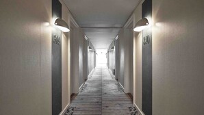 A long, narrow hotel corridor with numbers on the walls indicating room numbers, a patterned carpet, and wall-mounted lighting fixtures. - Four Points Flex by Sheraton Køge (Koge)