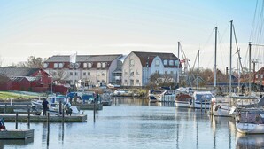 A marina with boats docked, a large white building with a flag, and a red barn in the background. - Four Points Flex by Sheraton Køge (Koge)
