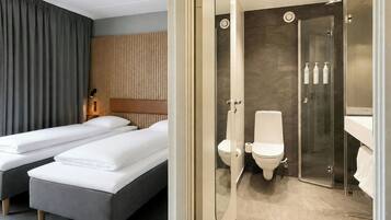 A hotel room with two beds, a wooden headboard, a large mirror, and a separate bathroom with a glass shower enclosure.