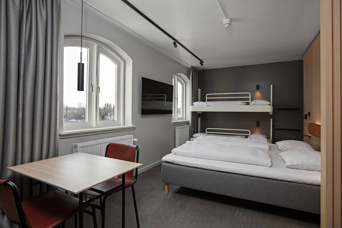 Ein modernes Hotelzimmer mit Etagenbett, einem Einzelbett, einem Tisch und einem Stuhl.
