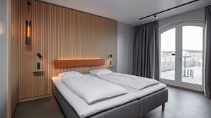 A modern hotel room with a large bed, a wooden slat wall, a sliding glass door to the balcony, and a small bedside table with a lamp. - Four Points Flex by Sheraton Køge (Koge)