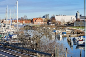 A marina with boats docked, a red building, and industrial structures in the background.