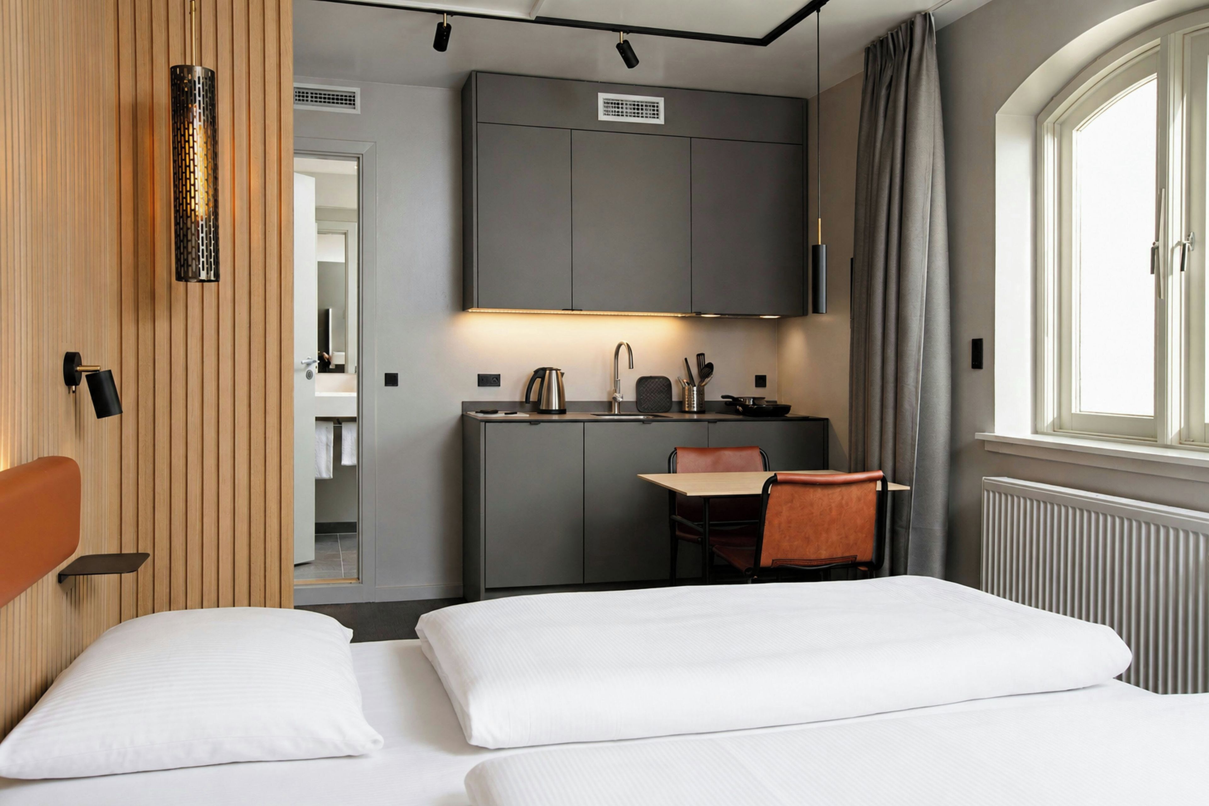 A hotel room with a bed, a desk, and a kitchenette.