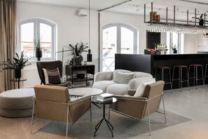 Una sala de estar moderna con un sofá, sillas, una mesa de centro y una zona de cocina con taburetes de bar.