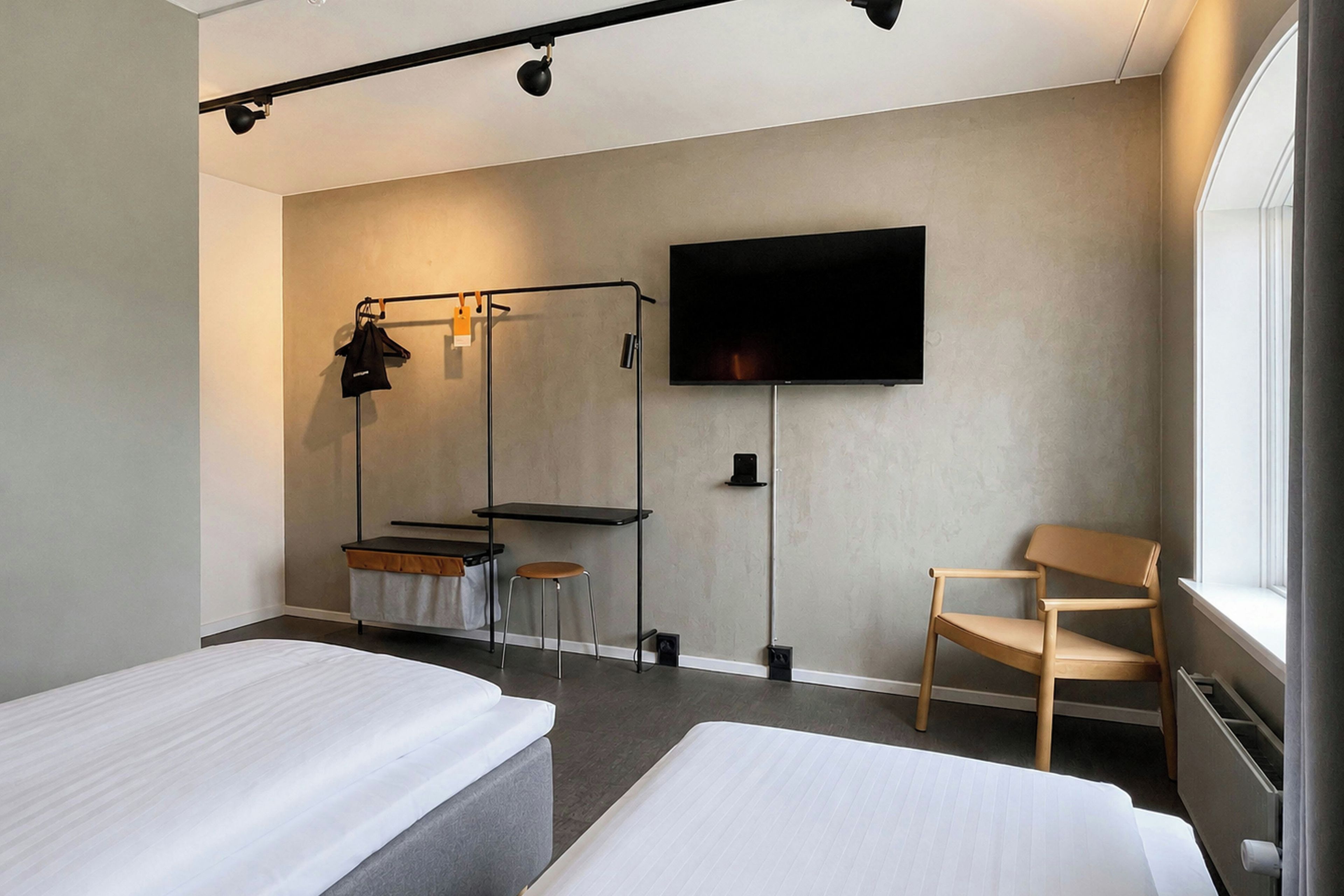 A hotel room with two beds, a TV, a chair, and a clothing rack.