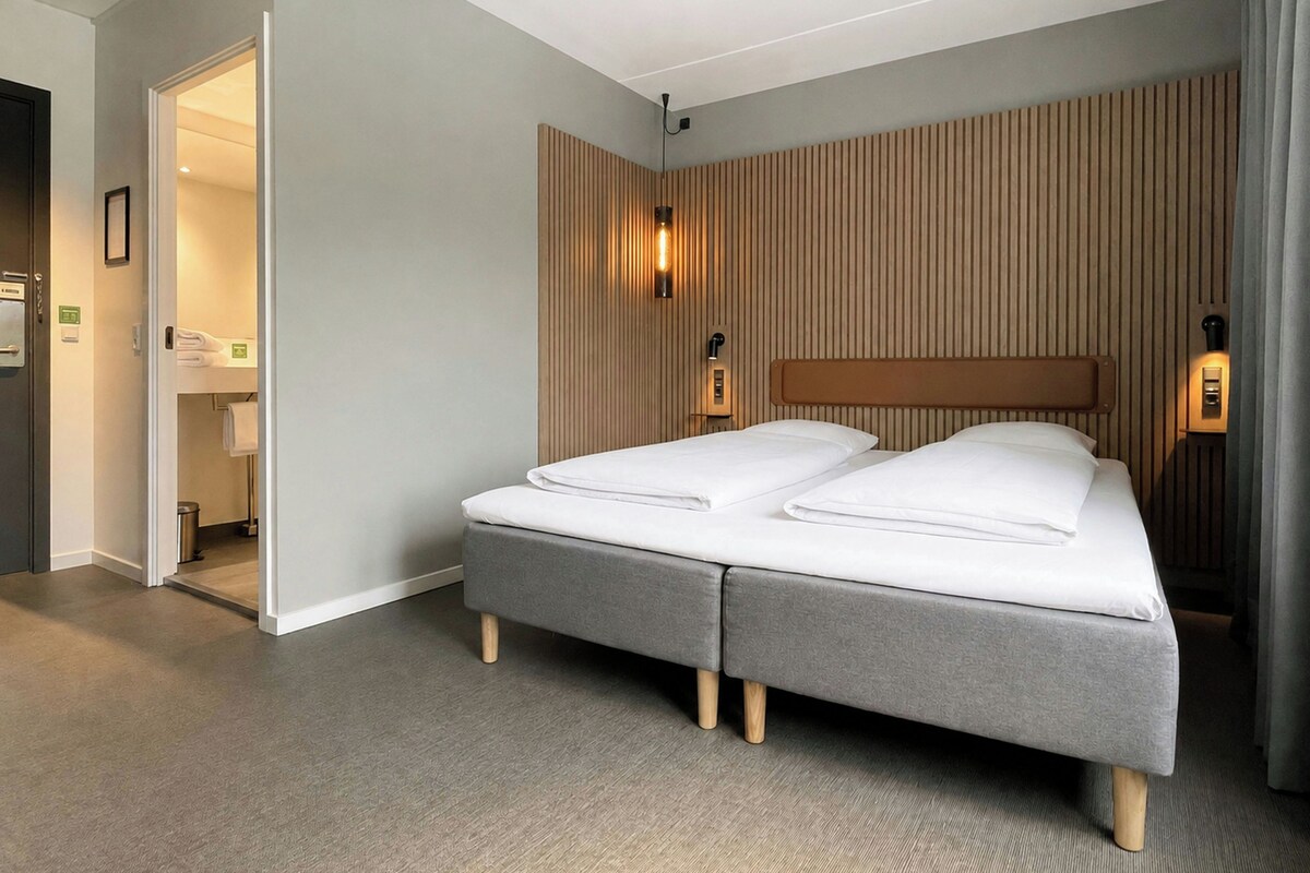 A modern hotel room with a grey bed, wooden headboard, and a wooden slat wall design.