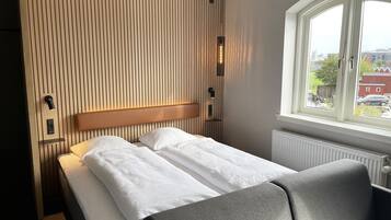 A hotel room with a bed, a bench, a window with a view, and a wall with vertical lines.