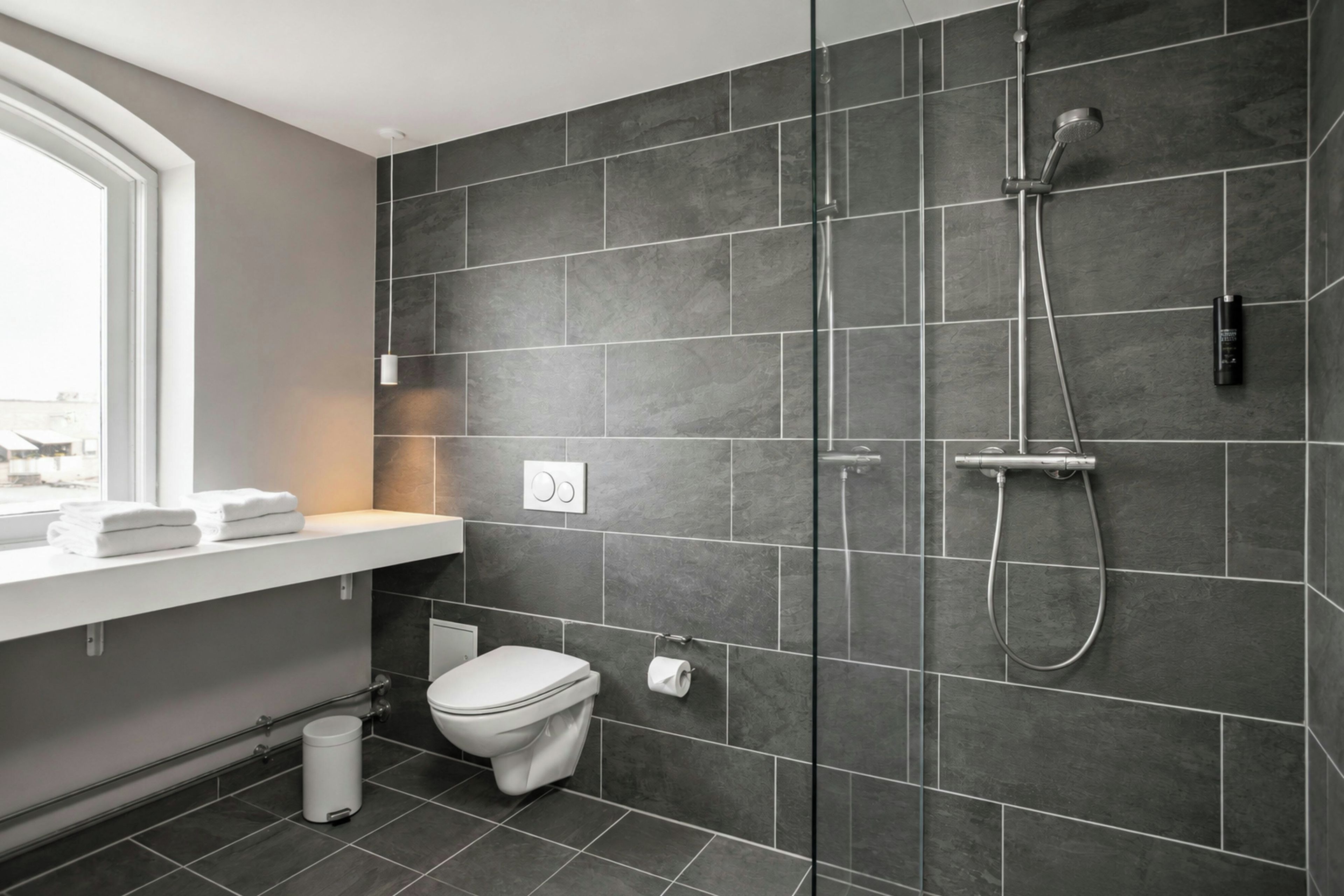 A modern bathroom with a shower, toilet, and a window.