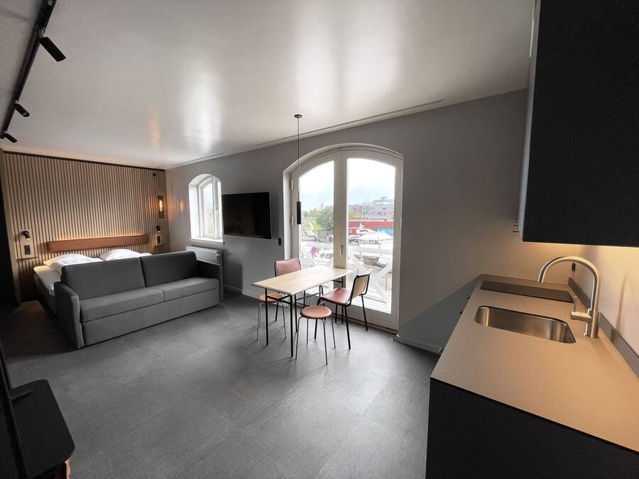 A modern kitchen with a dining area, a sofa, and a large window offering a view of the city.