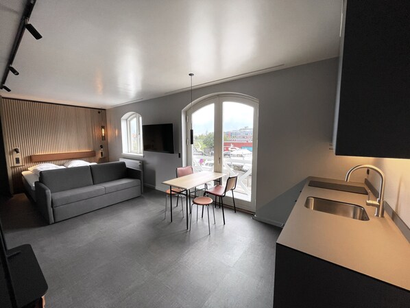 A modern kitchen with a dining area, a sofa, and a large window offering a view of the city. - Four Points Flex by Sheraton Køge (Koge)