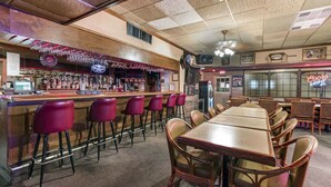 A bar area with a counter, bar stools, and a seating area with tables and chairs. - Lamplighter Inn & Suites - North (Springfield)
