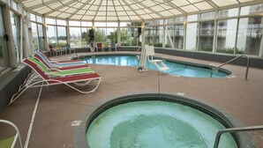 An indoor swimming pool with a glass ceiling, multiple lounge chairs, and a small hot tub. - Lamplighter Inn & Suites - North (Springfield)