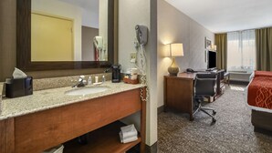 Un baño de hotel con lavamanos, espejo, secador de pelo y un escritorio con una silla.