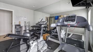 Un gimnasio equipado con cintas de correr, mancuernas y un banco.