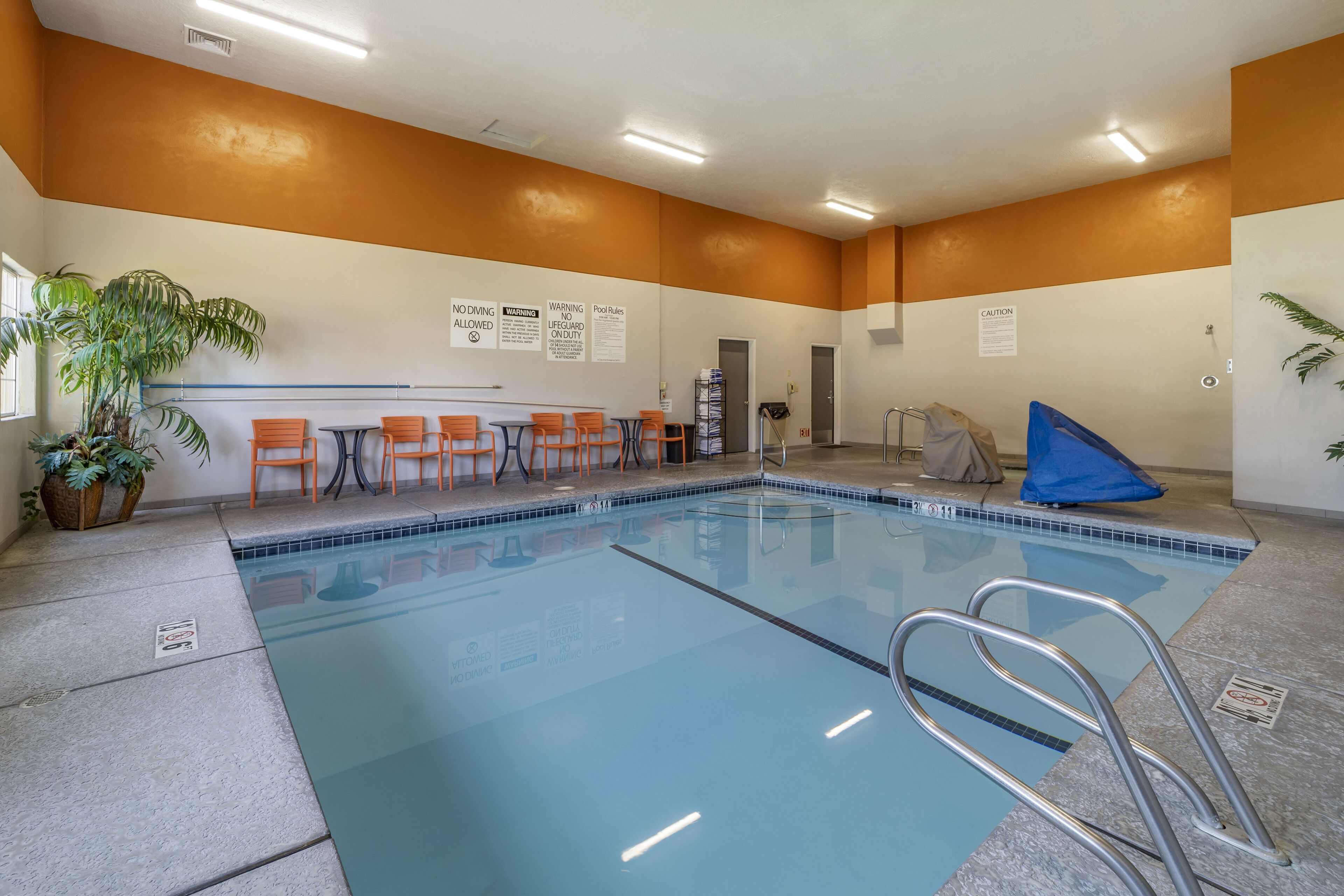 An indoor swimming pool with a tiled floor, surrounded by orange chairs and a blue lifeguard chair.