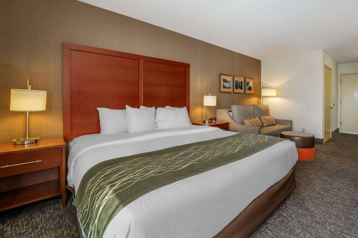 Ein Hotelzimmer mit einem großen Bett, zwei Nachttischen, einem Sessel, einem kleinen Tisch und einer Tür.