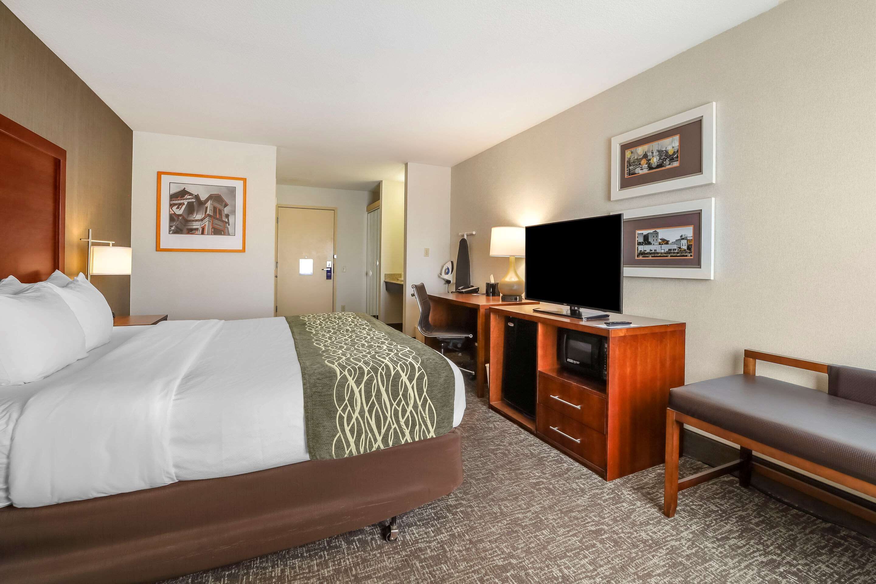 A hotel room with a bed, a desk with a television, a chair, and framed pictures on the wall.