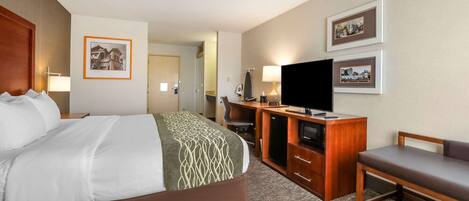 A hotel room with a bed, a desk with a television, a chair, and framed pictures on the wall.