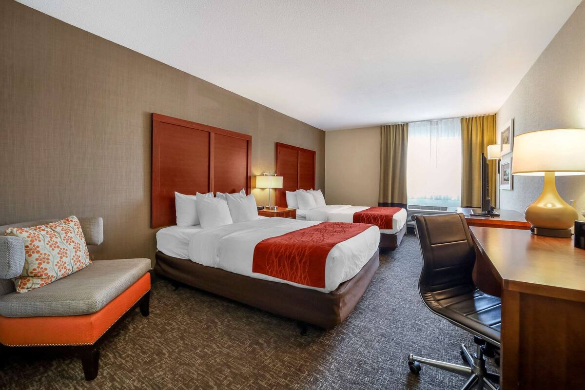 Ein Hotelzimmer mit zwei Betten, einem Schreibtisch, einem Sessel, einem Sofa und einer Lampe.