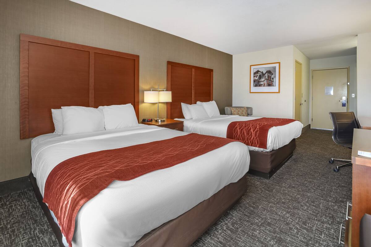 Ein Hotelzimmer mit zwei Betten, einem Schreibtisch, einem Stuhl und einer Lampe.
