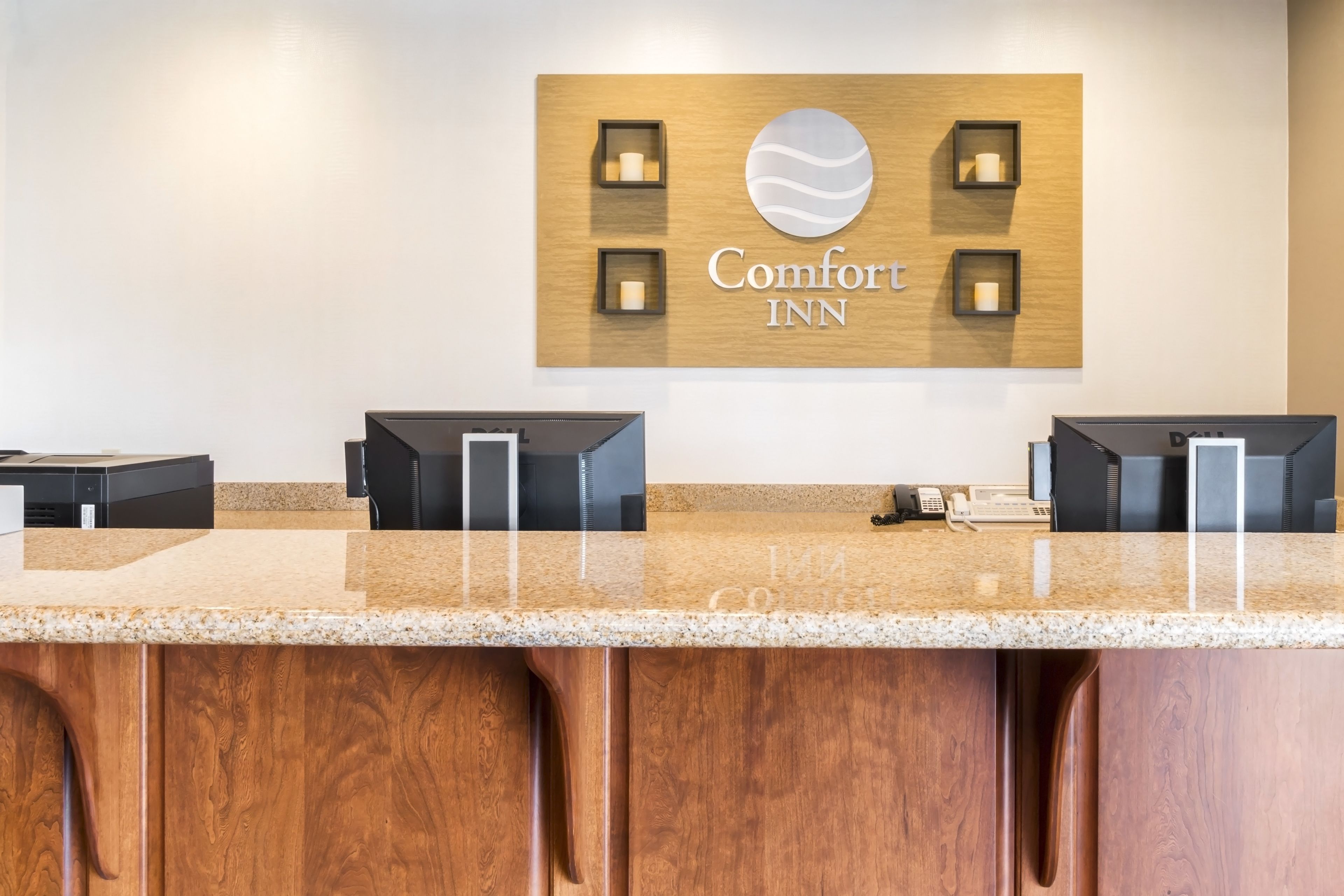 Eine Hotelrezeption mit einem hölzernen Verkleidungselement, das das Comfort Inn Logo, ein Telefon und eine Registrierkasse zeigt.