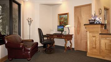 Une pièce comprenant un bureau en bois, un fauteuil en cuir, un ordinateur et un tableau encadré.