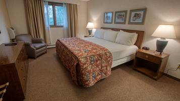 A hotel room with a large bed, two bedside tables with lamps, a chair, a desk, and a window with curtains.