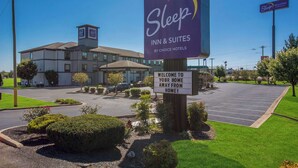 A Sleep Inn & Suites sign with a welcoming message, a parking lot, and a building with a flat roof. - Sleep Inn & Suites Cave City (Cave City)