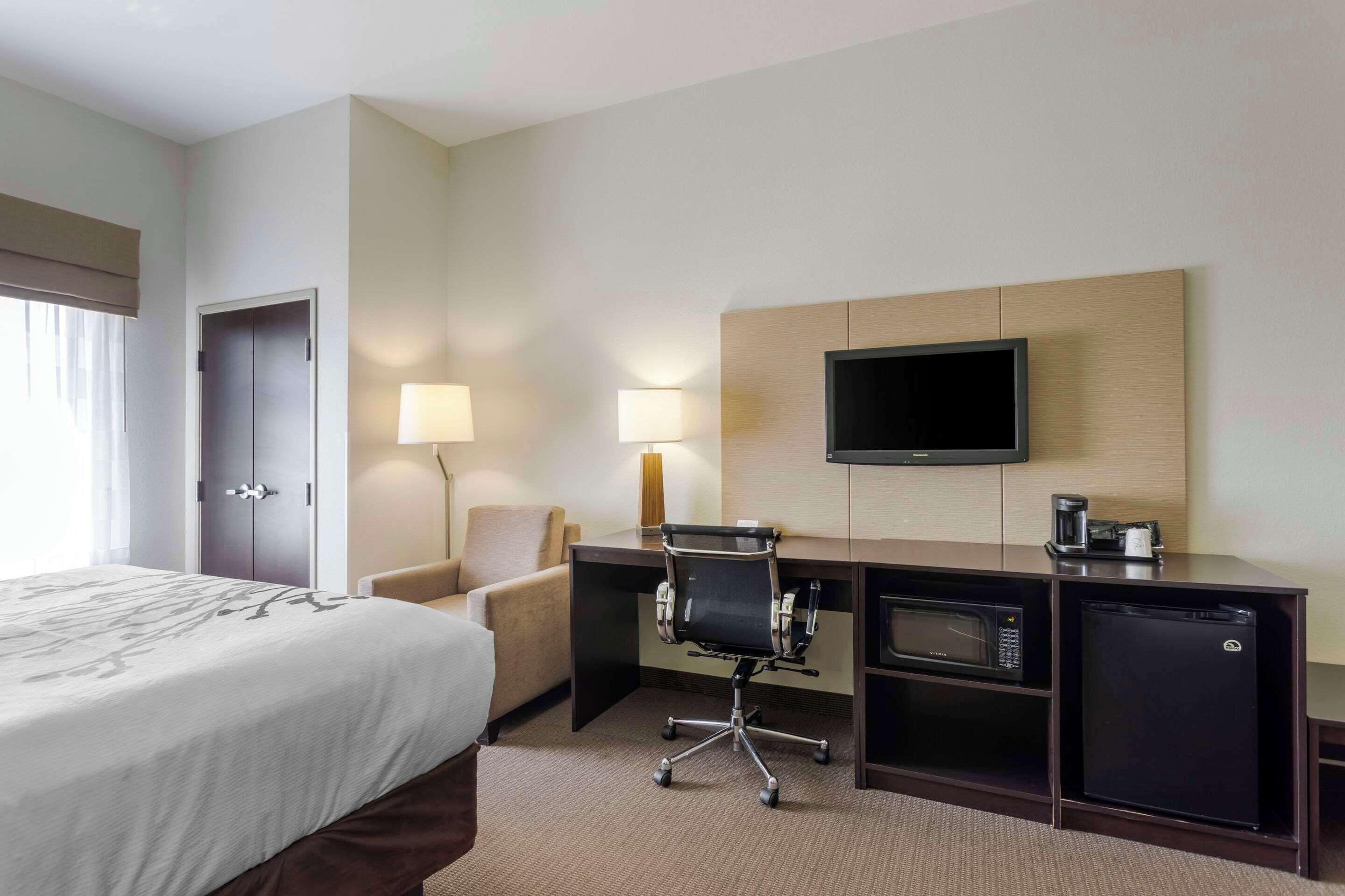 Una habitación de hotel con cama, escritorio, silla, televisión y cafetera.