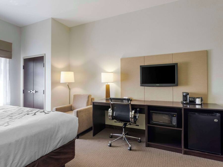 A hotel room with a bed, desk, chair, TV, and a coffee maker.