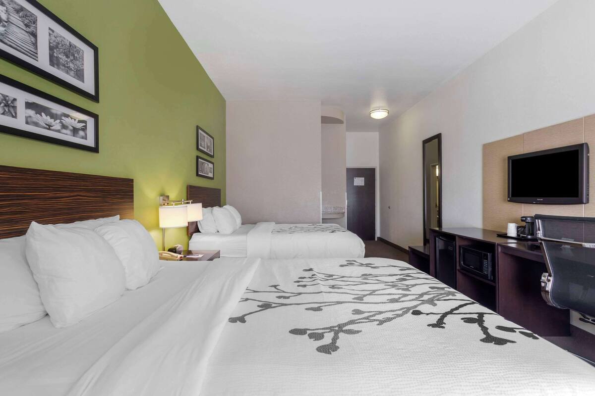 A hotel room with two beds, a desk with a flat-screen TV, a microwave, and a coffee maker.