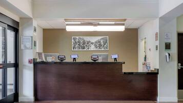 A reception desk with a dark wood finish, a welcome mat, and a wall-mounted artwork.