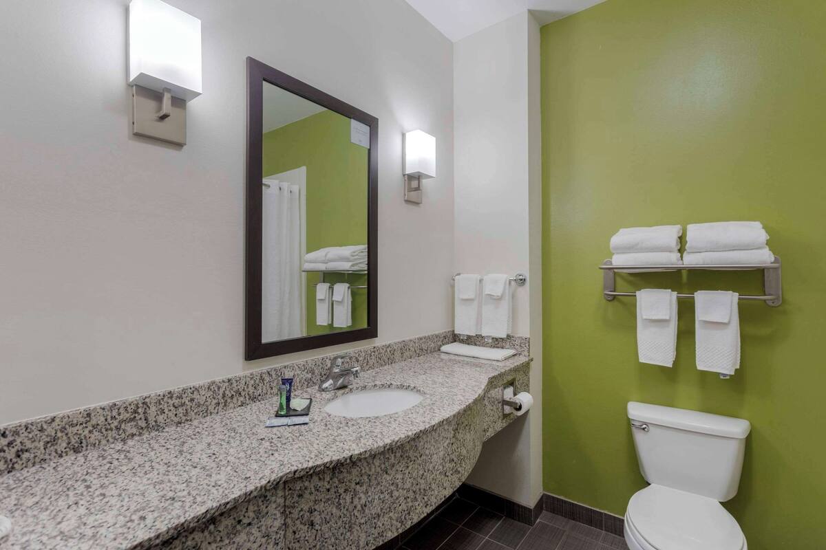 A bathroom with a granite countertop, a sink, a mirror, a toilet, and a towel rack.
