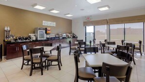 A modern dining area with tables and chairs, a kitchen counter with appliances, and large windows offering a view. - Sleep Inn & Suites Cave City (Cave City)
