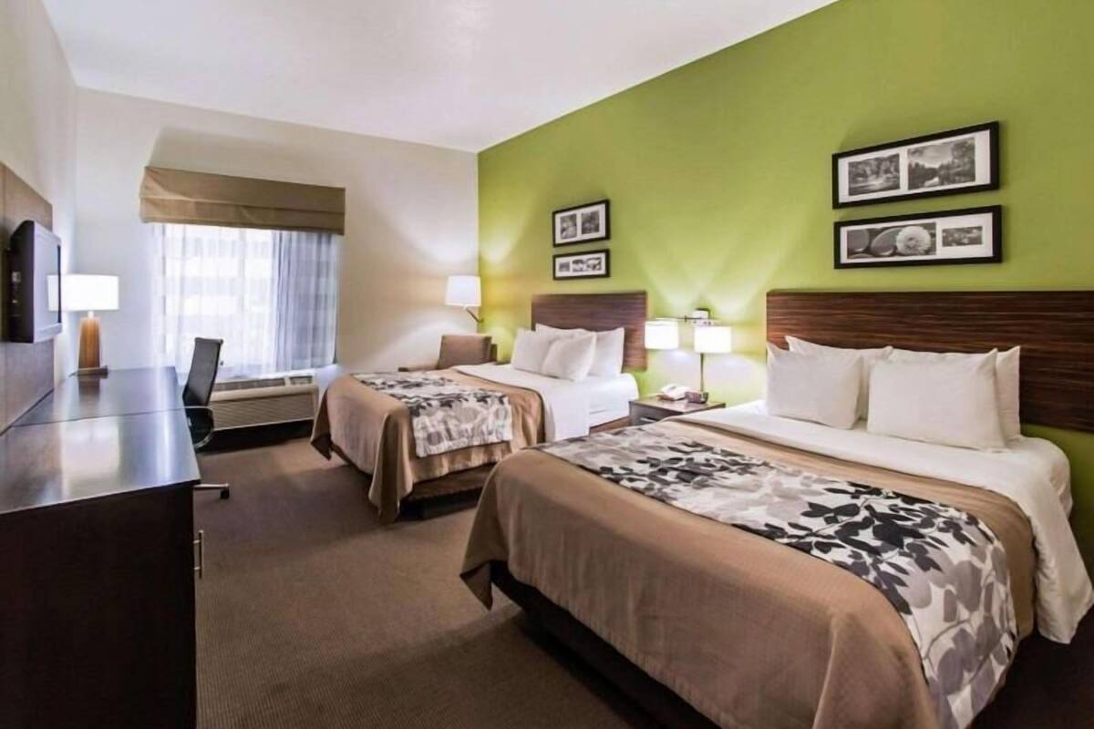 A hotel room with two beds, a desk, and a TV.