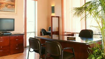 A hotel reception area with a desk, chairs, a television, and a large window with blinds.