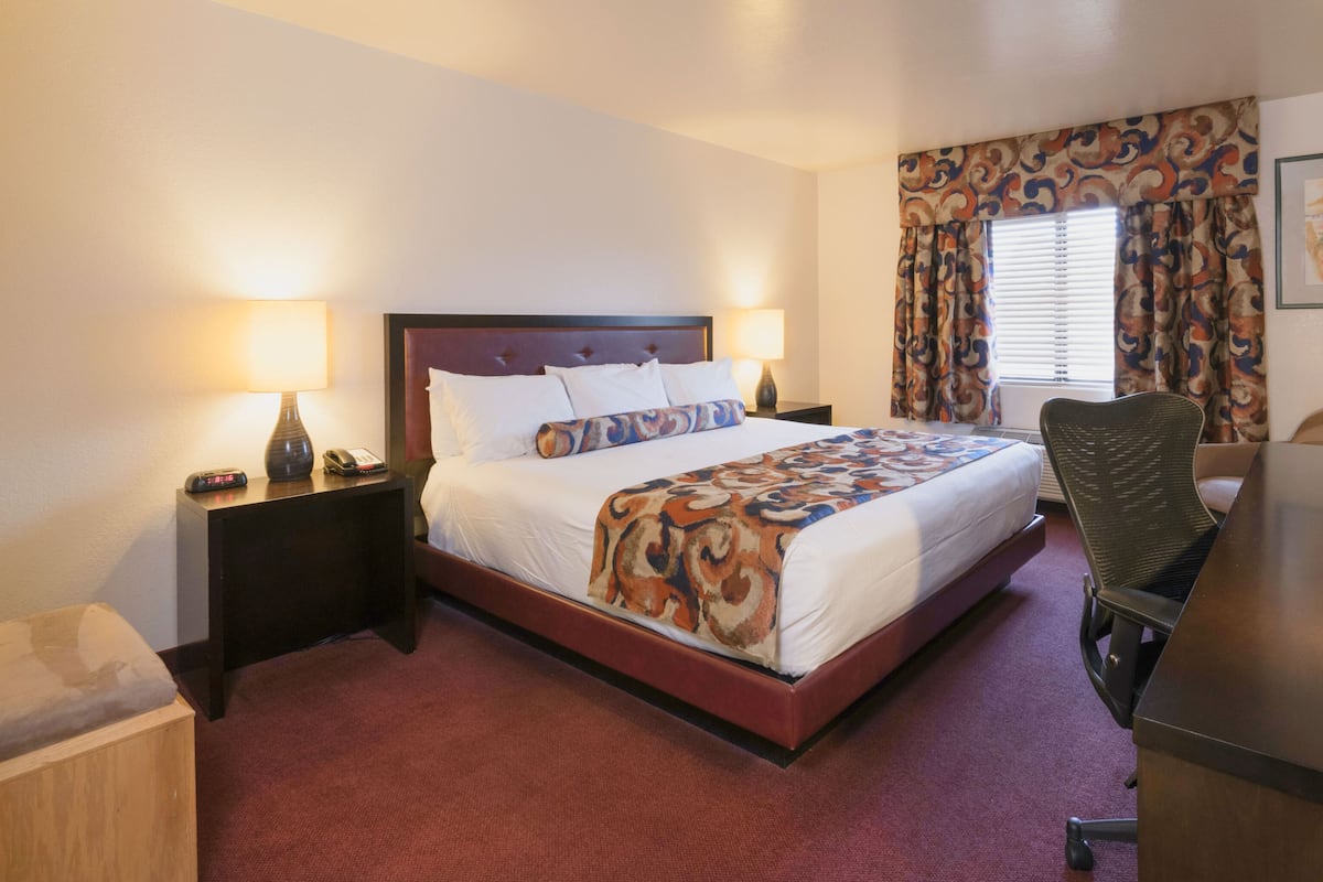 A hotel room with a bed, bedside lamps, a desk, a chair, and a window with curtains.