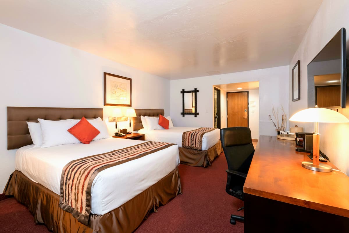 A hotel room with two beds, a desk, a chair, and a mirror.