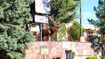 Señal del Grand Canyon Plaza Hotel con un letrero que indica restaurante de registro y una estatua de alce.