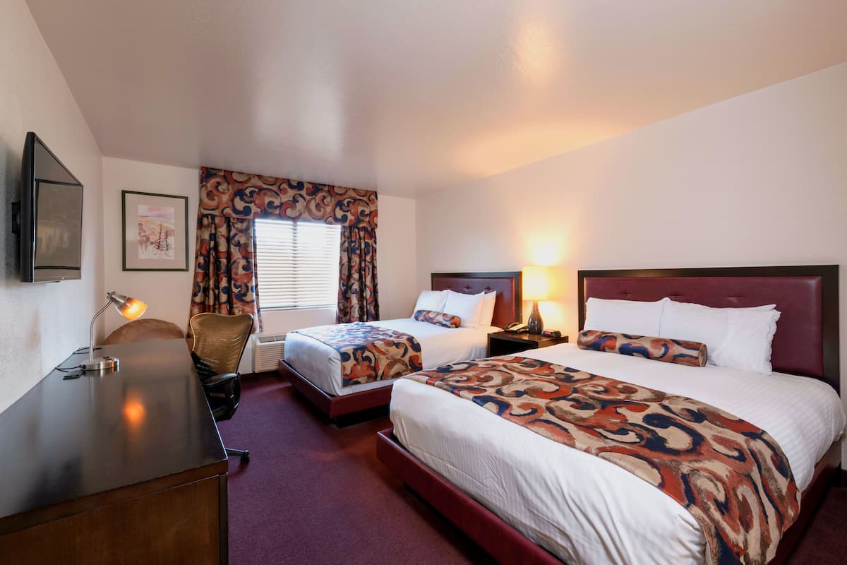 A hotel room with two beds, a desk, a chair, a TV, and a window with curtains.