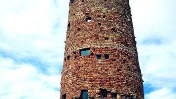 A tall, cylindrical stone tower with multiple windows, surrounded by a stone wall and vegetation.