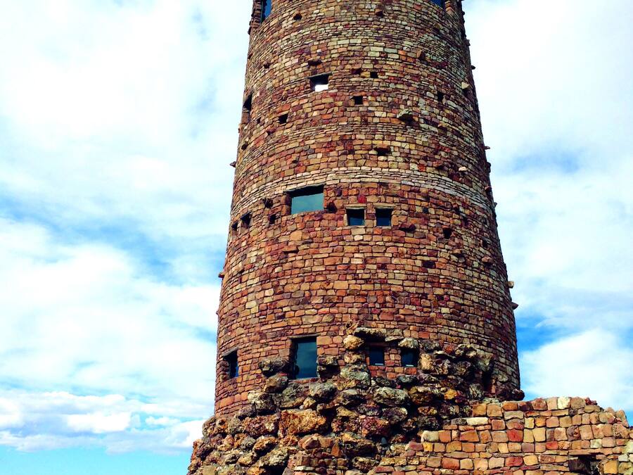 A tall, cylindrical stone tower with multiple windows, surrounded by a stone wall and vegetation.