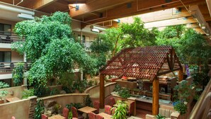 Een binnentuin met houten plafond, meerdere zithoeken en weelderige beplanting.