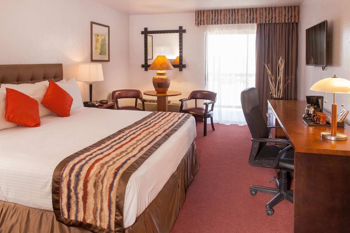 A hotel room with a bed, two chairs, a desk, a lamp, a coffee maker, and a TV.
